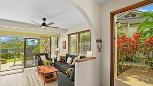 A spacious living room with a grey sofa, wooden coffee table, and a ceiling fan. - Summer Deal Poipu Beach Condo 5 Min Walk to Ocean Pools and Hot Tub (KOLOA)
