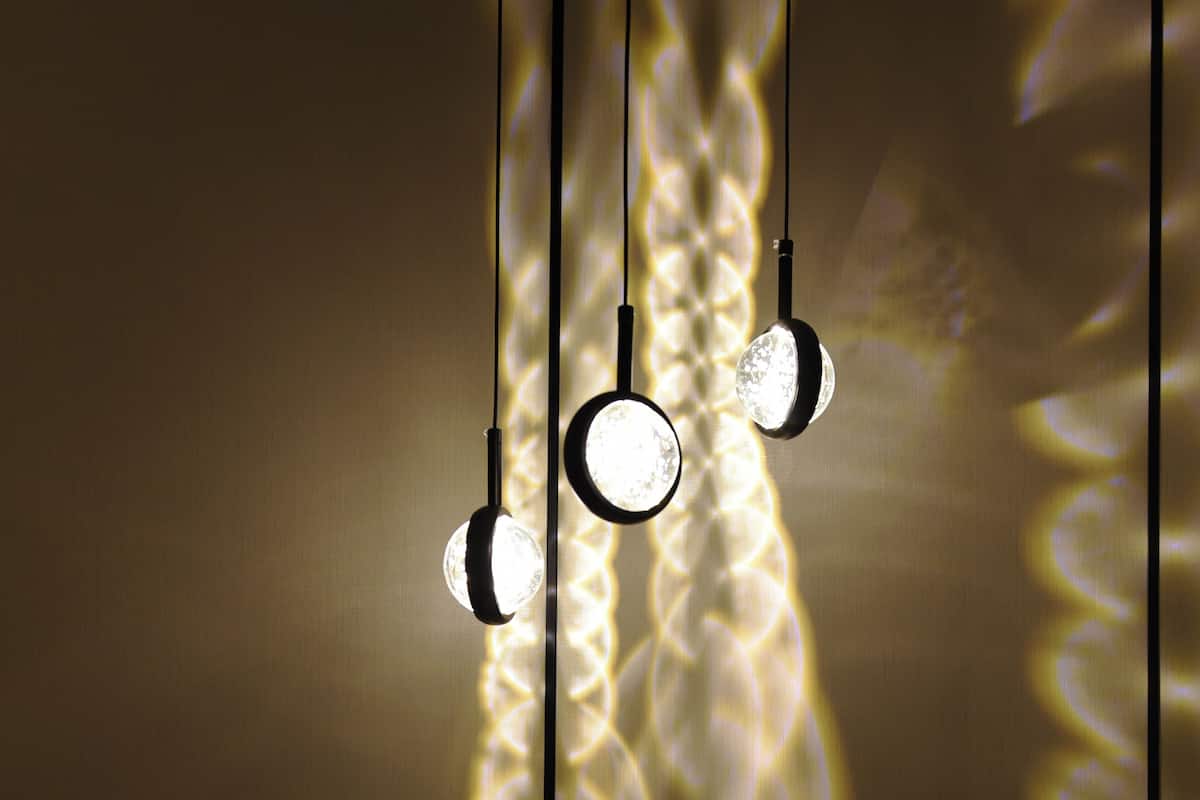 Three pendant lights with a textured wall in the background.