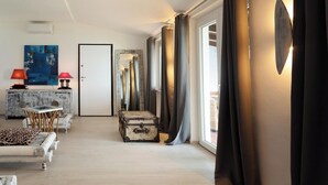 Ein modernes Wohnzimmer mit einer Couch, einem Tisch, einem Schrank und einem großen Spiegel. Eine Tür führt in einen anderen Raum, ein Fenster mit Vorhängen.