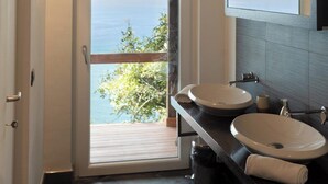 Ein Badezimmer mit zwei Waschbecken, einem großen Spiegel und Meerblick durch eine Glastür.