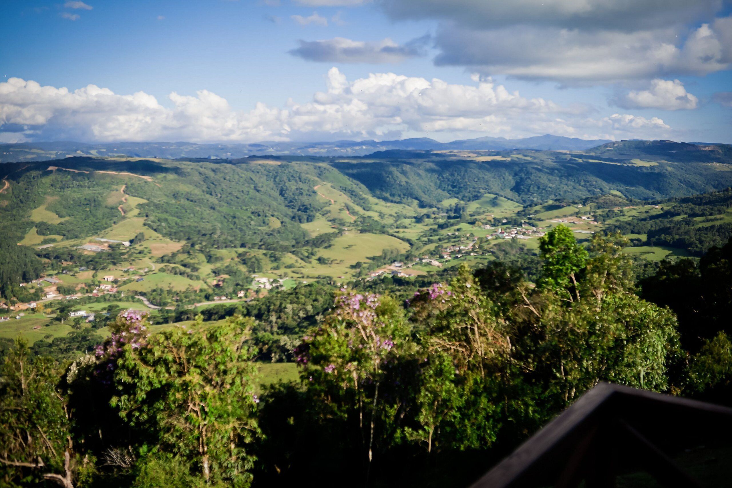 A panoramic view of a lush valley with rolling hills, a small village, and dense forested areas.