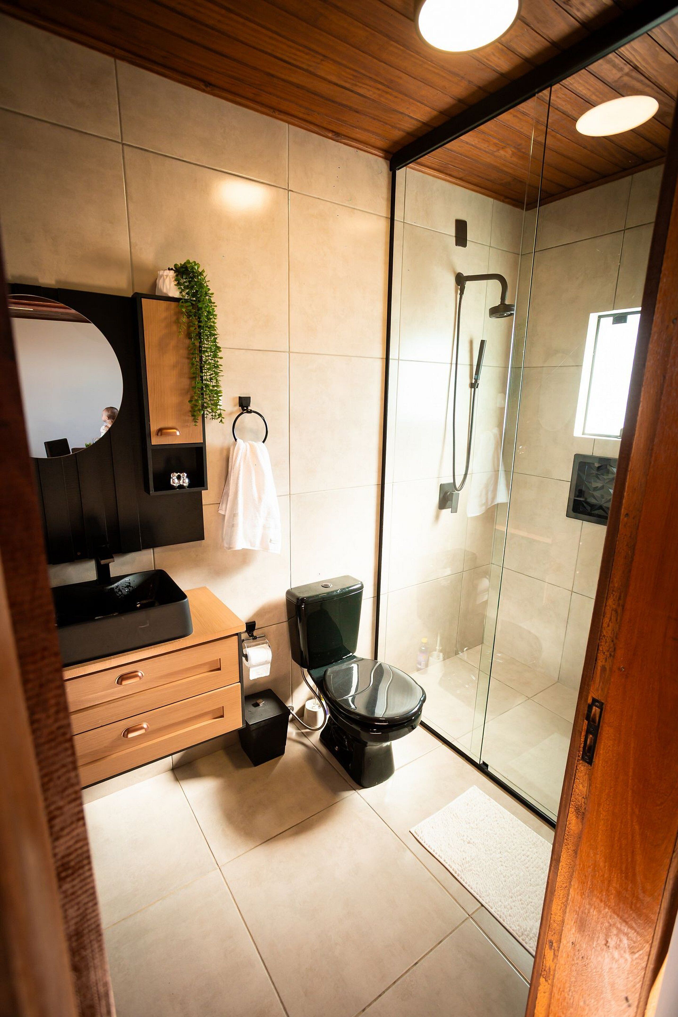 Un baño moderno con ducha de vidrio, inodoro negro, tocador de madera y espejo sobre el lavamanos.