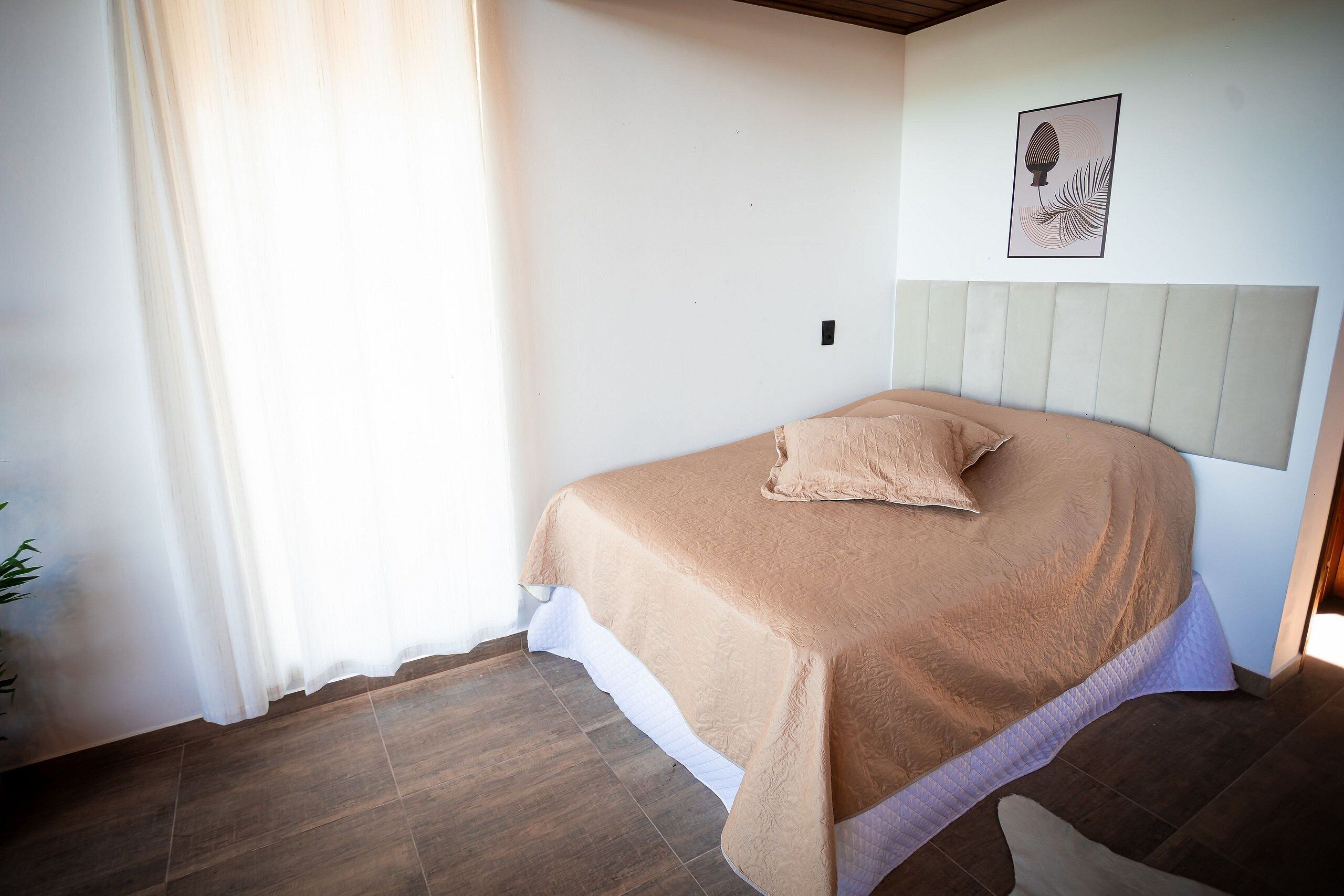 A bedroom with a bed, a headboard, a wall-mounted picture, and a window with curtains.