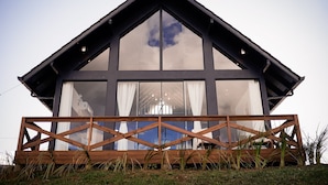 Uma casa moderna com telhado triangular, janelas amplas e um deck de madeira.