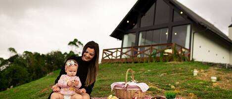 A picnic setup on a grassy area with a checkered blanket, a basket with food, and a building in the background.