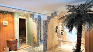 Een wellnessruimte met een houten wand, een beeld, een grote potplant en een vloer van mozaïektegels.