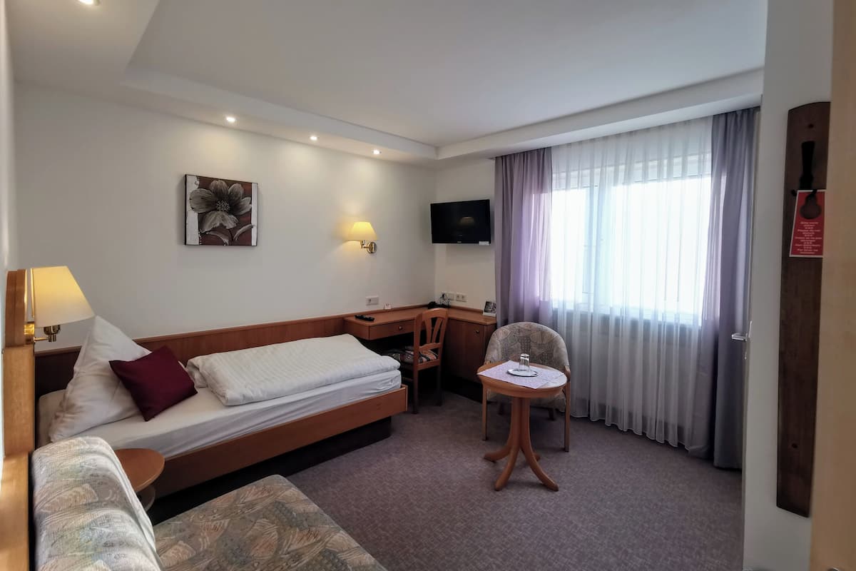 A hotel room with a bed, a desk, a chair, a TV, and a window with curtains.