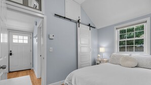 A bedroom with a bed, a window, a door, and a nightstand with a lamp.