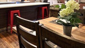 Eine moderne Küche mit weißen Schränken, einer Mikrowelle und einem roten Hocker. Es gibt einen Essbereich mit einem Holztisch und Stühlen, und eine Topfpflanze auf dem Tisch.
