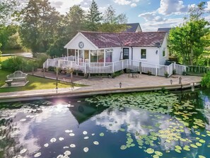 A white building with a red roof, a white fence, and a pond with lily pads. - 1 bedroom accommodation in Horning (Horning)
