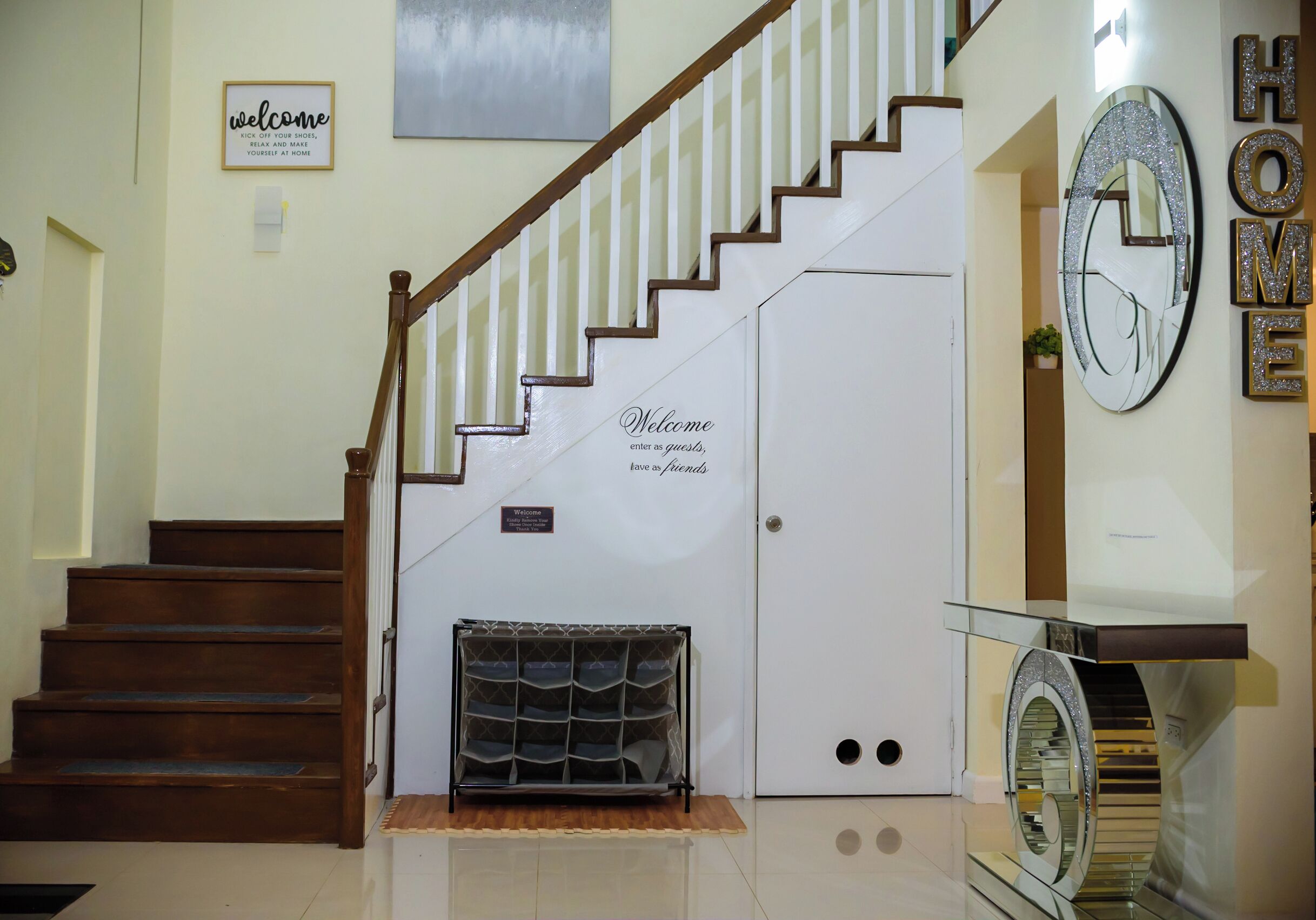 A staircase with a wooden handrail, a welcome sign, a coat rack, and a mirror with the word 'HOME' on the wall.