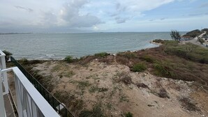 Vista costanera amb una platja sorrenca, cel serè i una ciutat llunyana a l'horitzó.