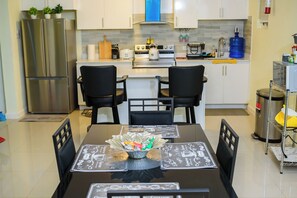 A modern kitchen with stainless steel appliances, a dining table with black chairs, and a water dispenser.