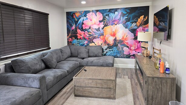 A modern living room with a sectional sofa, a wooden coffee table, and a vibrant floral mural on the wall.
