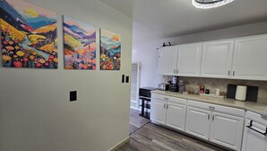 A modern kitchen with white cabinets, a countertop with appliances, and three colorful paintings on the wall.