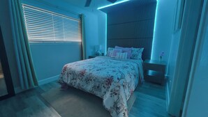 A bedroom with a bed, nightstands, a window with blinds, and a wall with vertical lines.