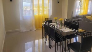 A dining area with a table, chairs, and yellow curtains. - Beachfront Bliss in Portmore – Stylish 1BR with Ocean Views & Modern Comfort (Portmore)
