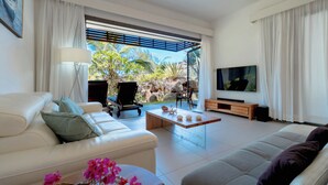 A modern living room with a white sofa, a grey sofa, a coffee table, a TV, and a view of the outdoors. - Beachfront chic retreat (Belle Mare)