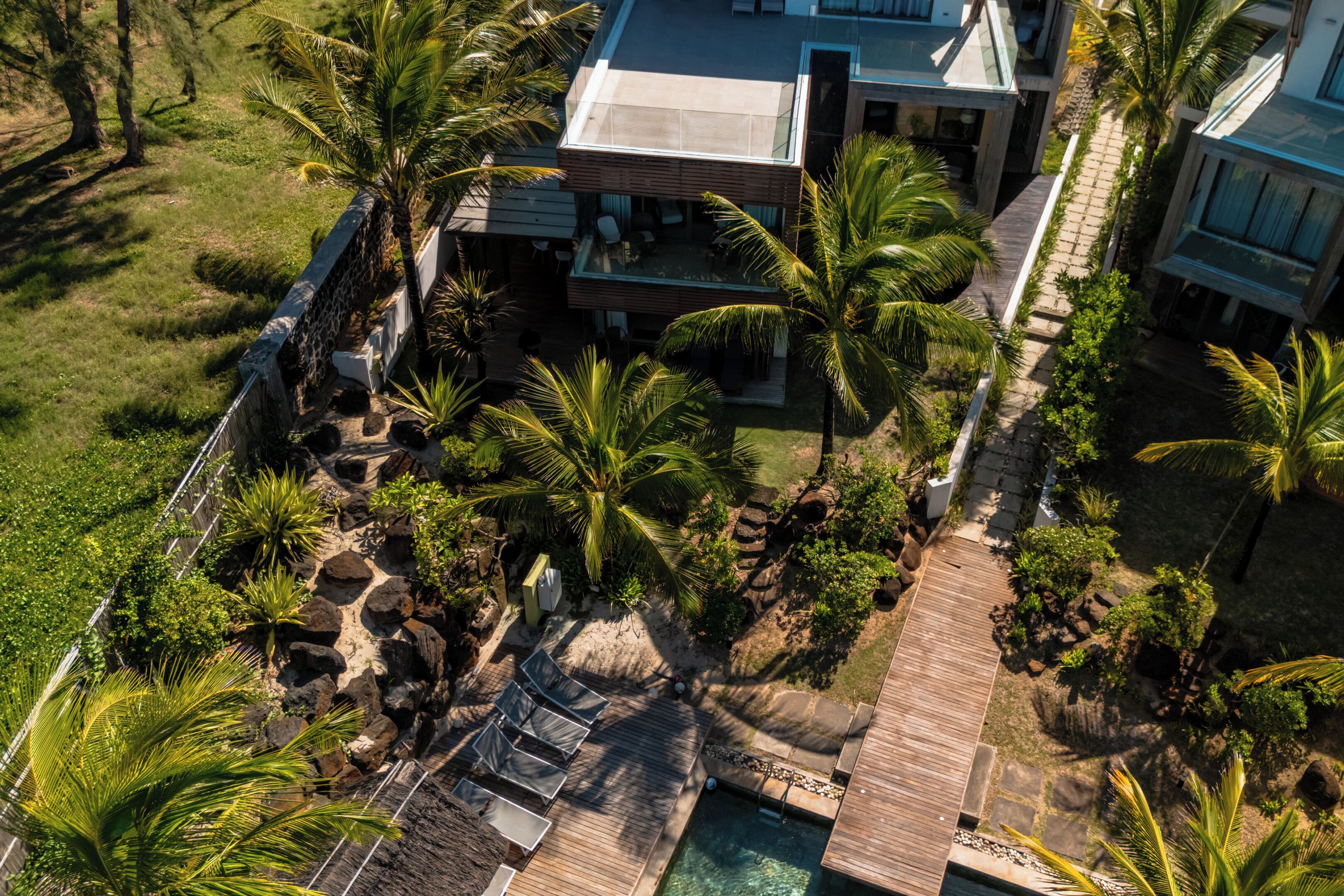 An aerial view of a modern resort with a pool, lounge chairs, and palm trees.