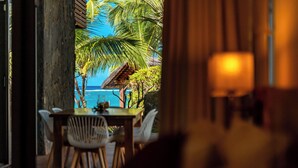 A dining area with a view of the ocean and palm trees. - Beachfront chic retreat (Belle Mare)