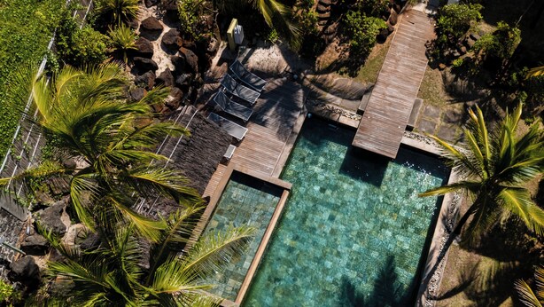 An aerial view of a resort with a clear pool, wooden deck, and palm trees. - Beachfront chic retreat (Belle Mare)