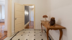 Un pasillo con una puerta de madera, suelo de baldosas y una mesa de madera con un jarrón y una escultura.