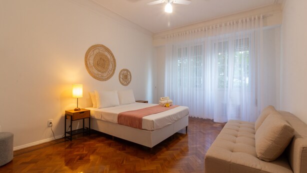 Un dormitorio con cama, mesita de noche, lámpara y sofá.