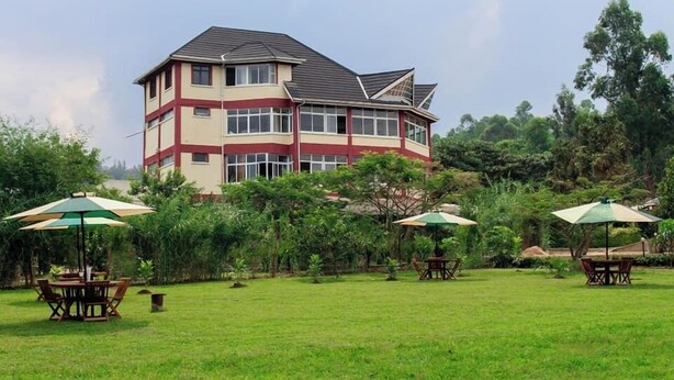 A two-story building with a flat roof and multiple windows. There are outdoor tables and chairs with umbrellas. - Balance Park Hotel  (Kisumu)
