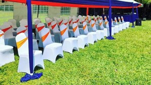 A tented outdoor event space with rows of white chairs, some with orange sashes, and a grassy area. - Balance Park Hotel  (Kisumu)