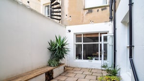 Une petite cour avec un banc en bois, des plantes en pot et une fenêtre donnant sur une pièce.