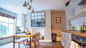 Une cuisine moderne avec un plancher en bois, un coin repas avec une table et des chaises en bois, et une grande fenêtre qui laisse entrer la lumière naturelle.
