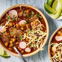 Un tazón de estofado con carne, frijoles y rábanos, adornado con hierbas.