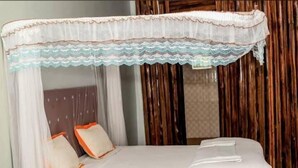 A bed with a white canopy and orange pillows, a wooden headboard, and a patterned wall. - rwabs legacy motel mubende (Mubende)