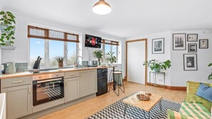 Ett modernt kök med en inbyggd ugn, en diskho och en matplats med barstolar. Det finns krukväxter och inramade tavlor på väggarna.