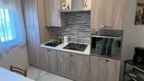 A modern kitchen with wood cabinetry, a gas stove, an oven, and a small dining area with a table and chairs. - LITTLE HOUSE (Fossarmato)
