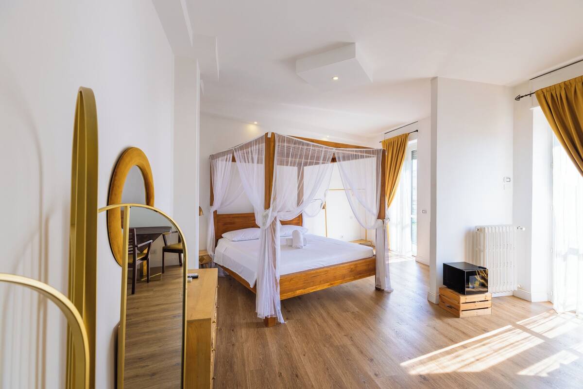 A spacious bedroom with a wooden bed, a large mirror, and a small TV on a wooden crate.