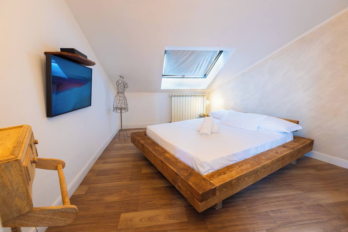 A bedroom with a wooden bed, a TV mounted on the wall, a skylight, and a radiator.
