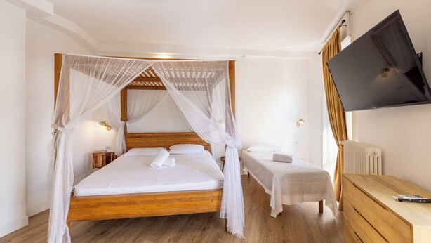 Une chambre à coucher avec un lit à baldaquin en bois, une table de chevet et une petite table d’appoint, ainsi qu’un téléviseur fixé au mur.