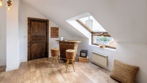 Une chambre située dans un espace de type « loft », avec un plafond en pente, une porte en bois, un petit coin bar avec des tabourets, un radiateur et une vue à travers un puits de lumière.