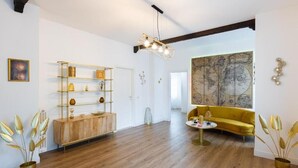Une pièce spacieuse avec un plancher en bois, un canapé jaune, une bibliothèque à la dorure et une carte accrochée au mur.