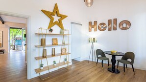 Un intérieur moderne avec un plancher en bois, une décoration en forme d’étoile, un panneau indiquant « Bonjour », une table ronde avec des chaises et un luminaire suspendu.