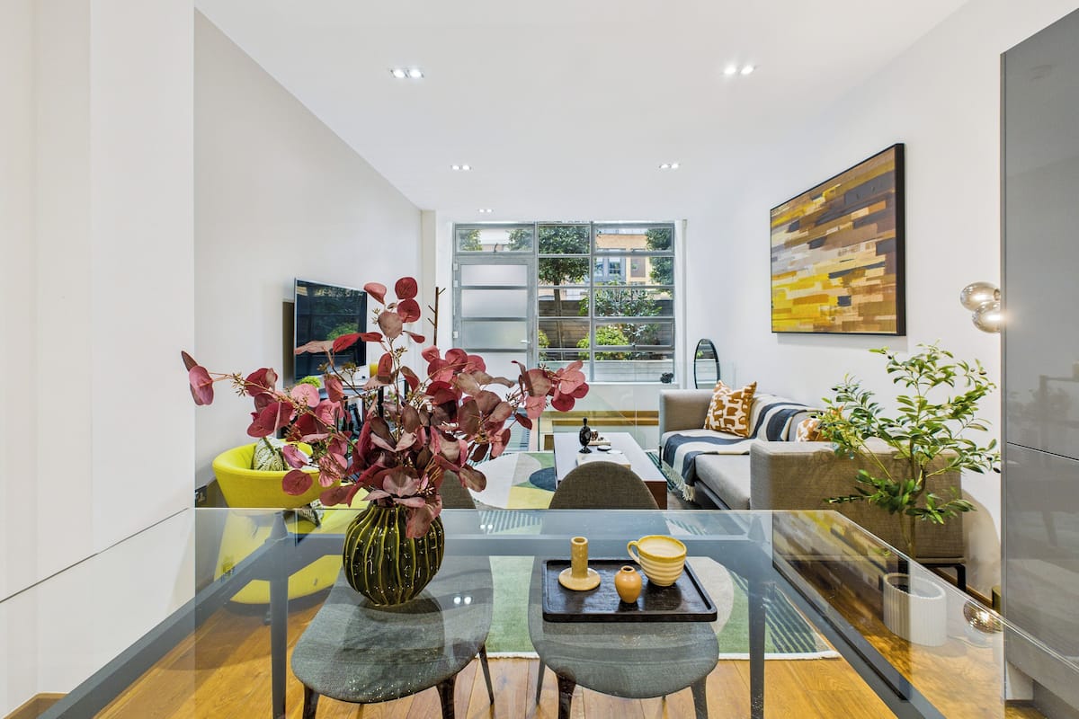 Una sala de estar moderna con una mesa de vidrio, un sofá y una mesa de centro. Hay un ventanal con vistas al exterior.