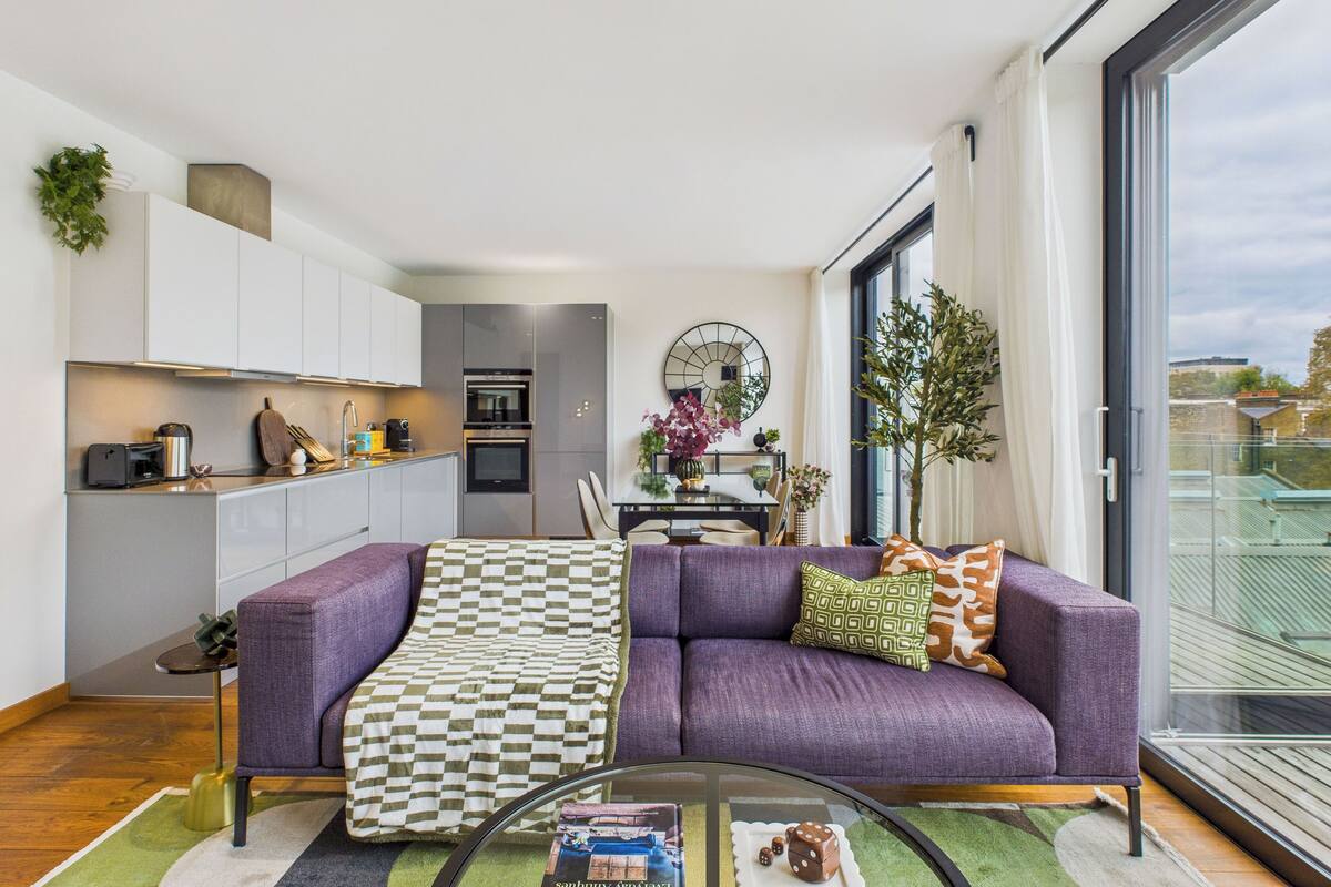 Un apartamento moderno con un sofá morado, una manta a cuadros y una zona de comedor con mesa de vidrio.