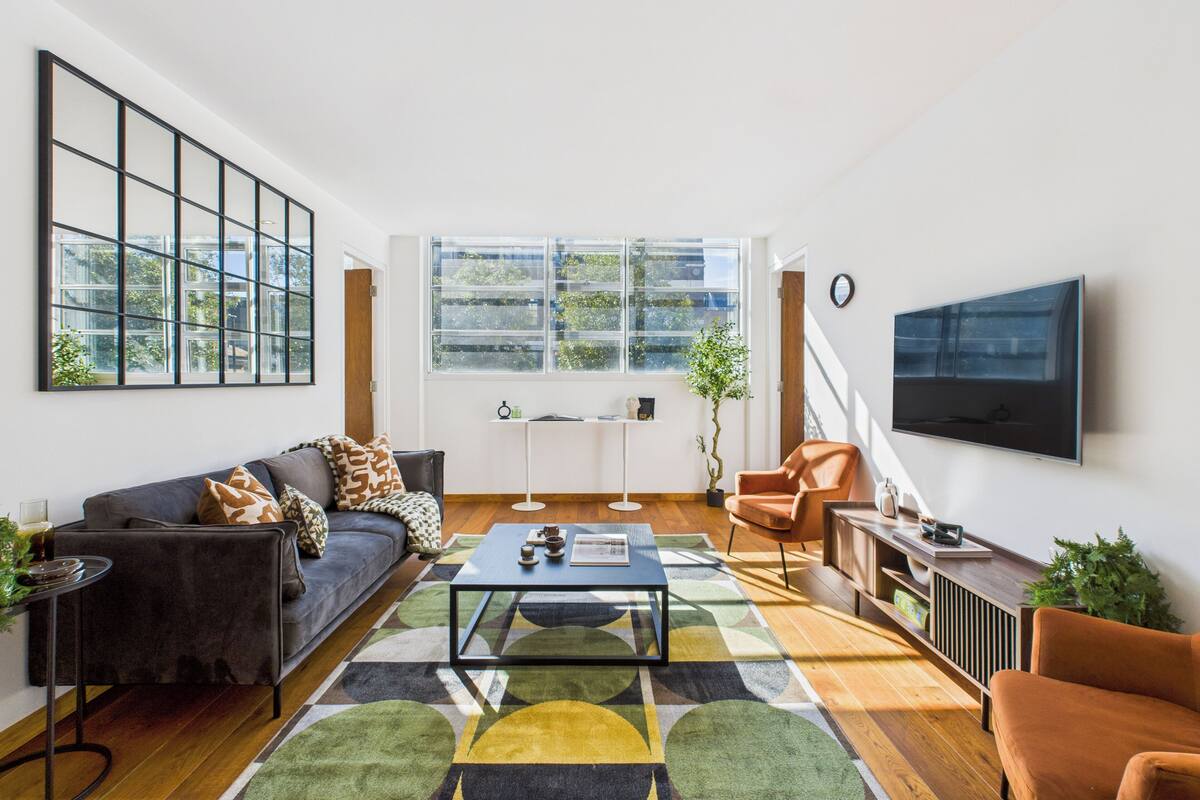 Una sala de estar moderna con un sofá, un sillón, una mesa de centro y un televisor montado en la pared.