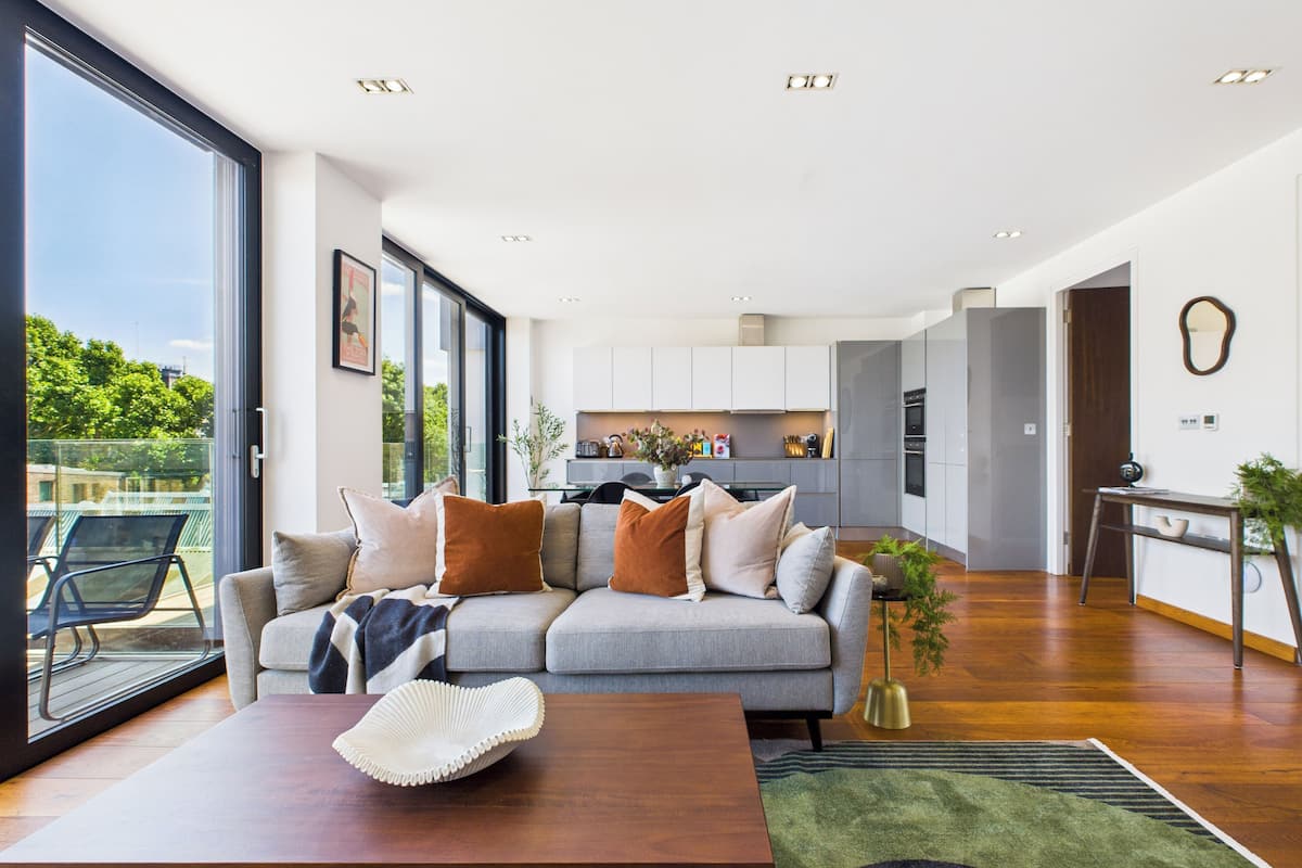 Una sala de estar moderna con un sofá gris, una mesa de centro de madera y vistas a la cocina y al área exterior.