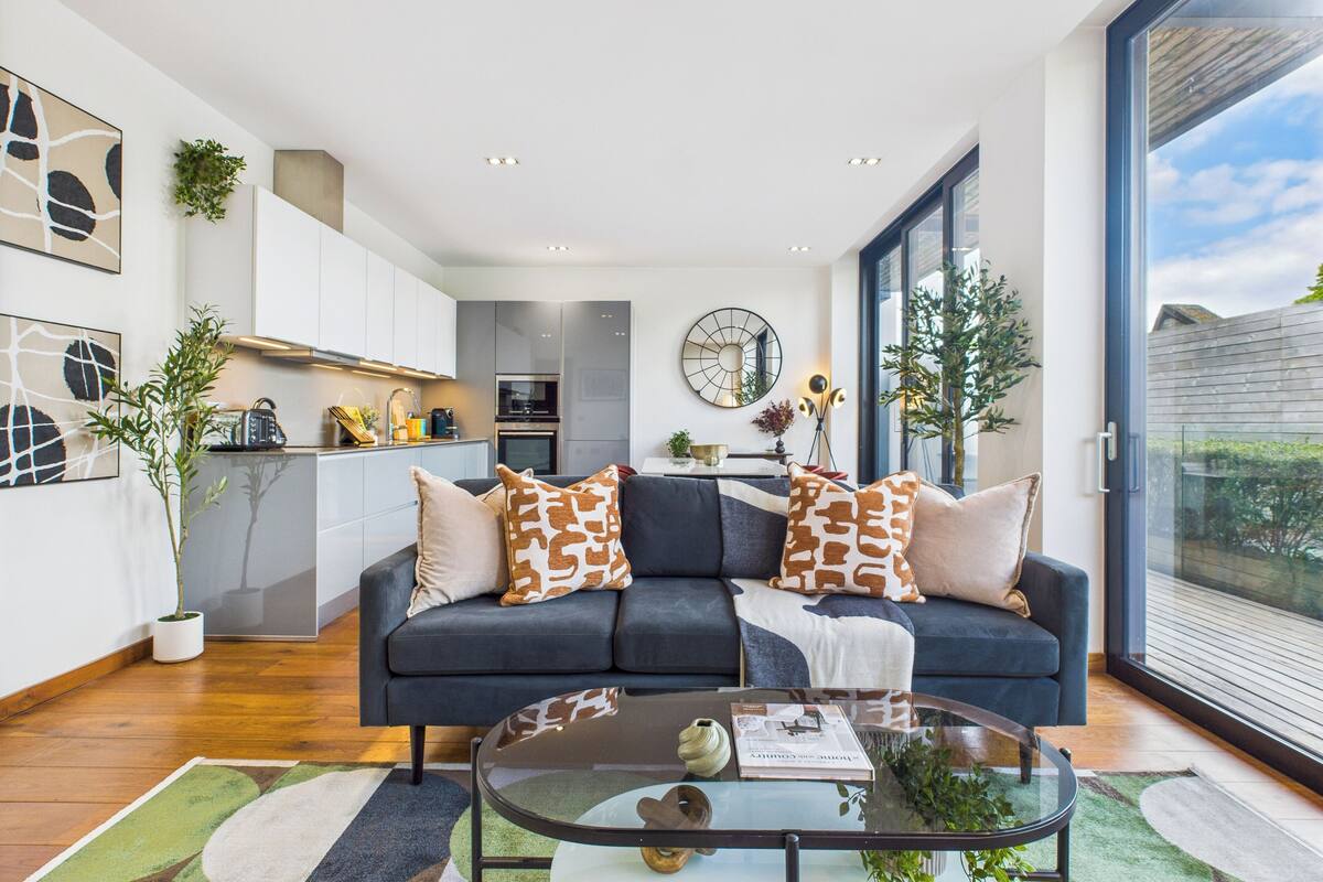 Una sala de estar moderna con un sofá oscuro, una mesa de centro de vidrio y vistas al exterior.