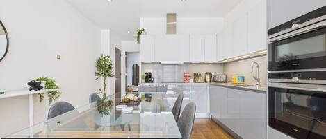 Una cocina moderna con armarios blancos, una mesa de comedor de cristal y dos sillas grises.