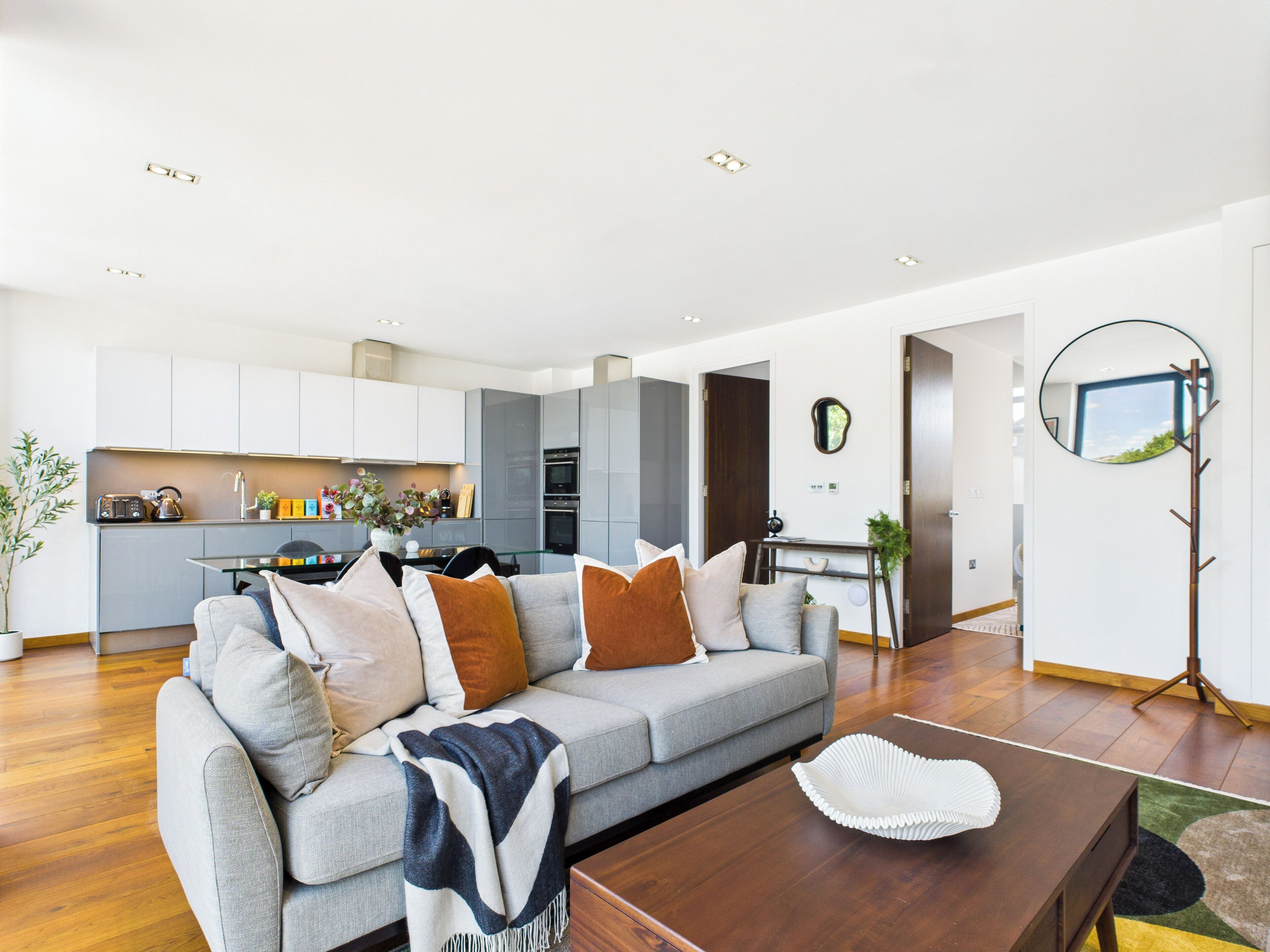 Una sala de estar moderna con un sofá gris, una mesa de centro de madera y una cocina al fondo.