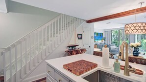 A modern kitchen with a wooden staircase, a large island, and a view of the living area. - Villa 407 - Beautiful 2 Bedroom Retreat (Jekyll Island)