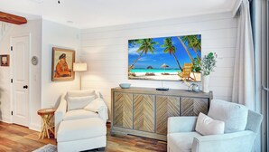 A modern living room with a large TV, white sofas, a wooden herringbone cabinet, and a beach-themed painting. - Villa 407 - Beautiful 2 Bedroom Retreat (Jekyll Island)